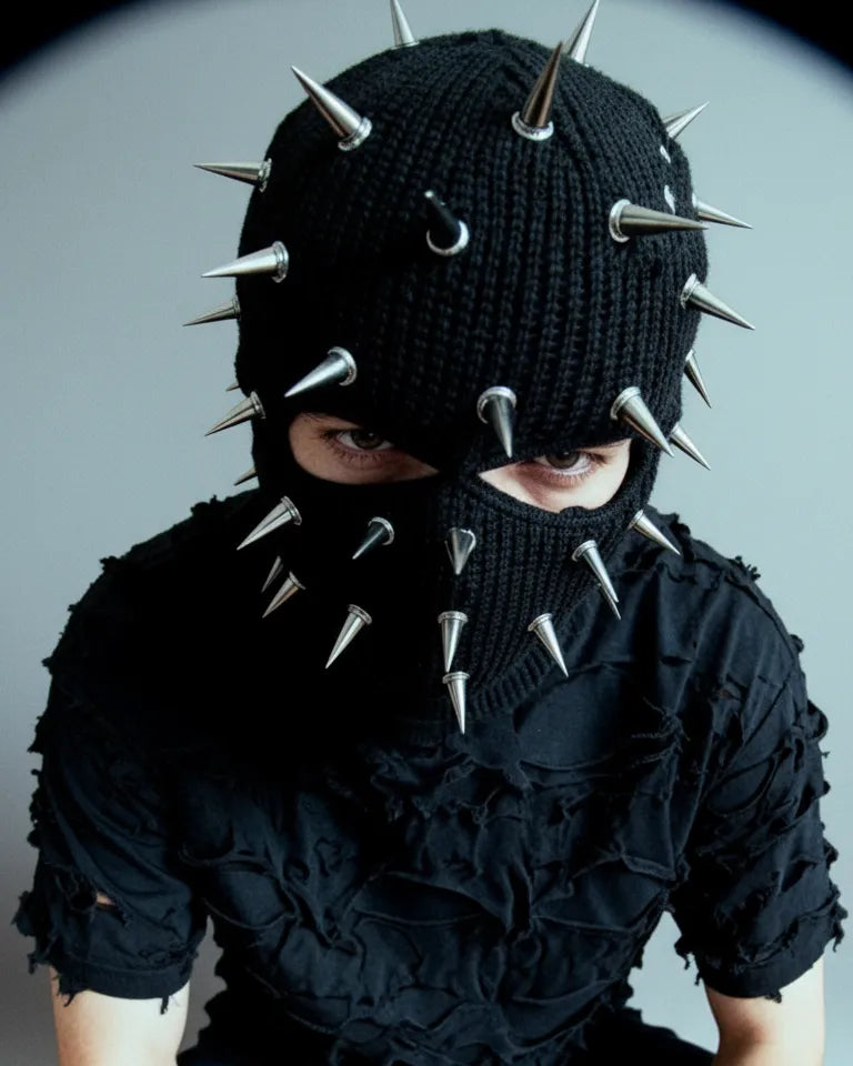 Photoshoot of a techno artist wearing a punk hood masking his face in cotton with metal spikes and a ripped black t-shirt.