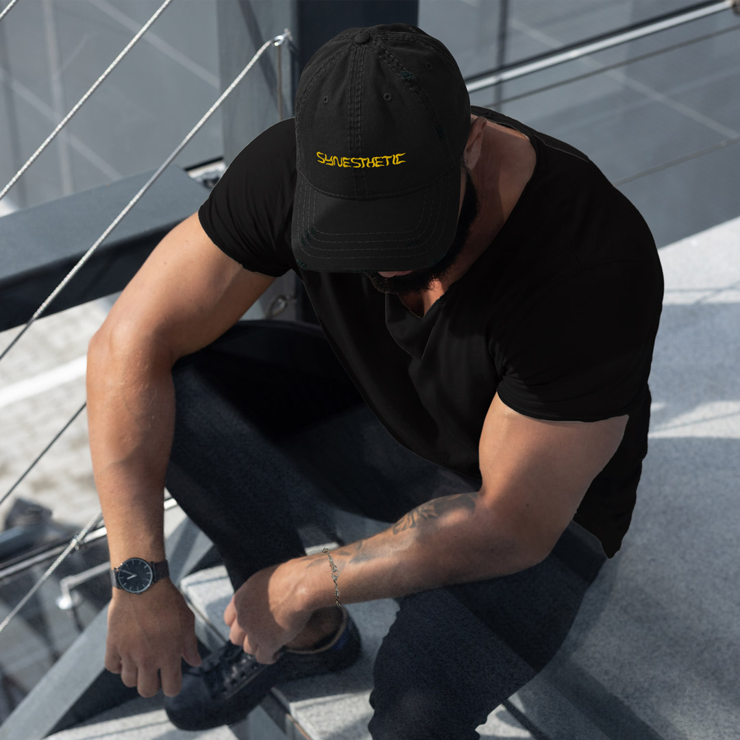 un homme portant une casquette noir avec le logo Synesthetic brodé en jaune sur le devant